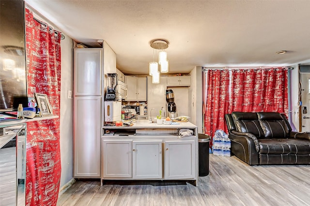 kitchen featuring hanging light fixtures, light hardwood / wood-style flooring, white cabinets, and a textured ceiling