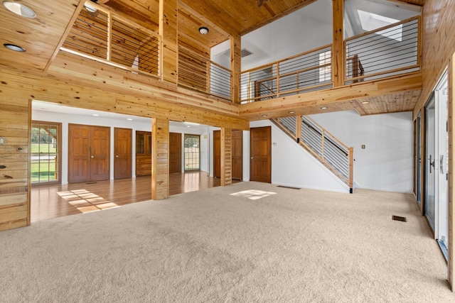 unfurnished living room with wood ceiling, light colored carpet, wooden walls, and a high ceiling