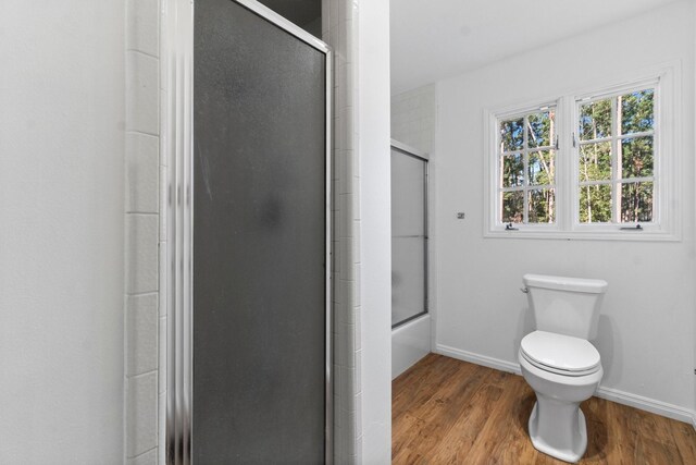 bathroom featuring combined bath / shower with glass door, hardwood / wood-style floors, and toilet