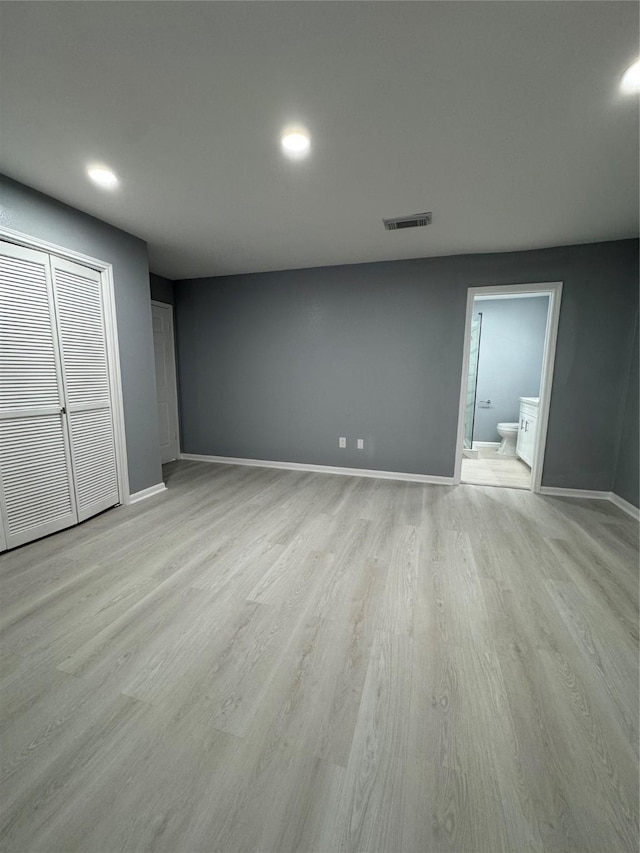 unfurnished bedroom featuring connected bathroom, light wood-type flooring, and a closet