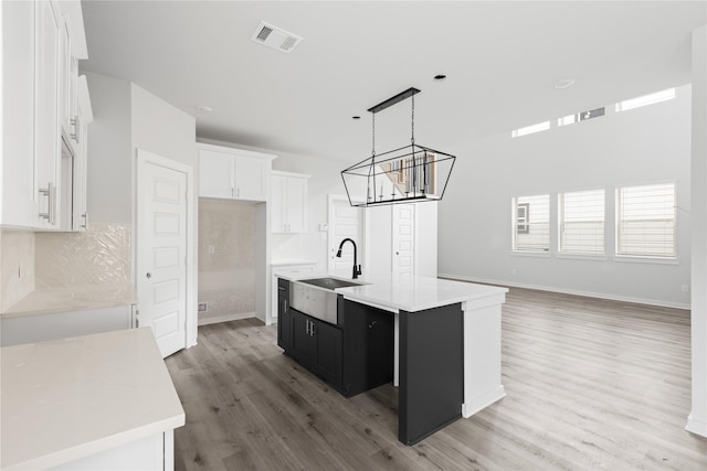 kitchen with sink, white cabinetry, decorative light fixtures, light wood-type flooring, and an island with sink