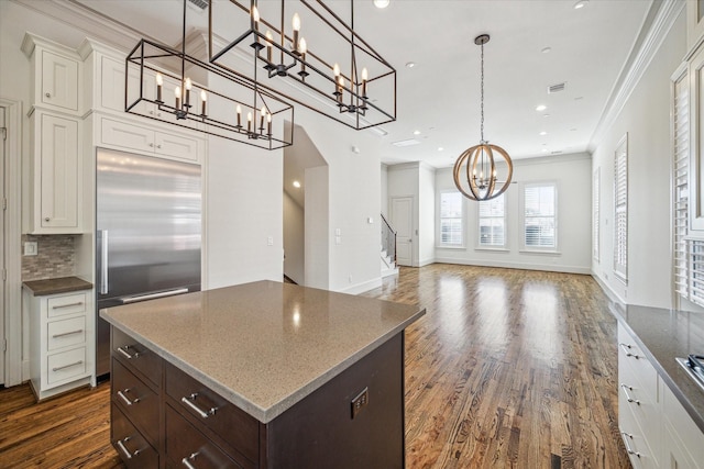 kitchen with decorative light fixtures, a center island, stainless steel built in fridge, dark brown cabinetry, and crown molding