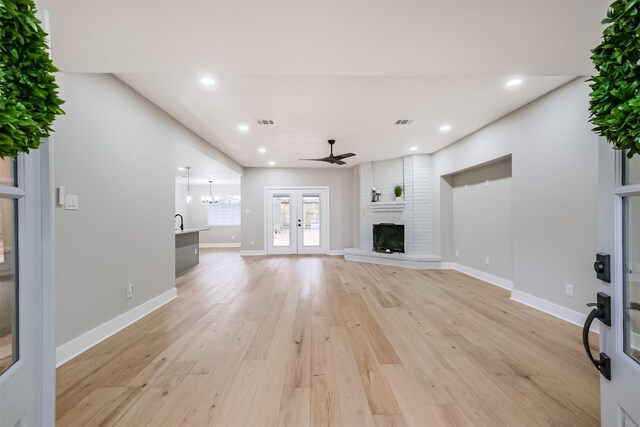 unfurnished living room featuring ceiling fan, light wood-type flooring, a fireplace, and french doors