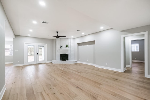 unfurnished living room with french doors, a brick fireplace, ceiling fan, and light hardwood / wood-style flooring