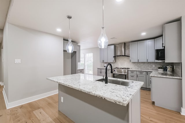 kitchen featuring pendant lighting, wall chimney range hood, sink, gray cabinets, and an island with sink