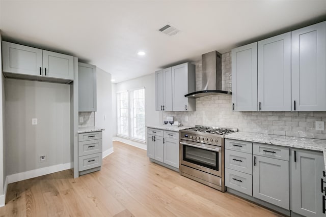 kitchen with light stone counters, light hardwood / wood-style flooring, stainless steel range with gas cooktop, decorative backsplash, and wall chimney range hood