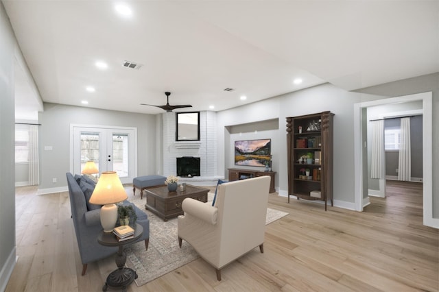 living room with french doors, ceiling fan, a fireplace, and light hardwood / wood-style floors