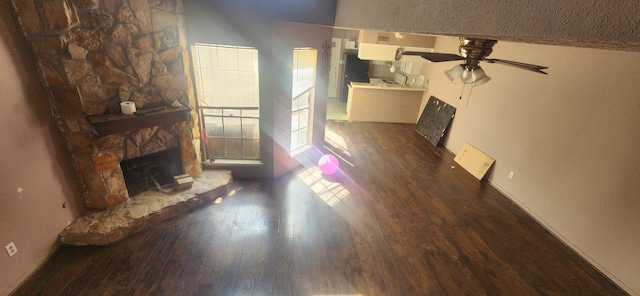 unfurnished living room featuring dark hardwood / wood-style flooring, a stone fireplace, and ceiling fan