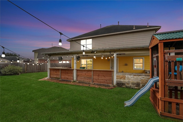 back house at dusk with a playground and a lawn