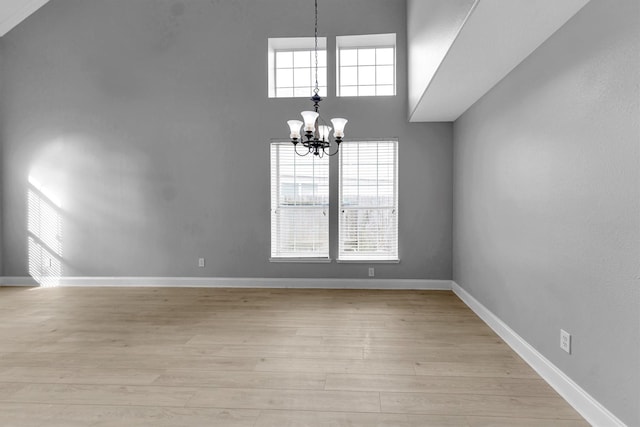 spare room featuring an inviting chandelier, a high ceiling, and light wood-type flooring