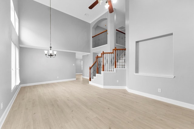 unfurnished living room with a high ceiling, ceiling fan with notable chandelier, and light wood-type flooring