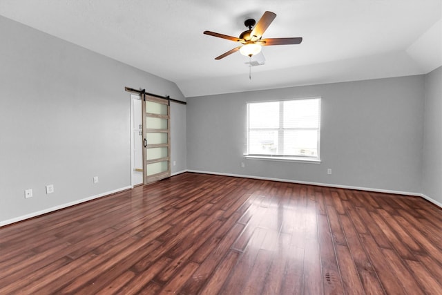 empty room featuring ceiling fan, a barn door, lofted ceiling, and dark hardwood / wood-style flooring