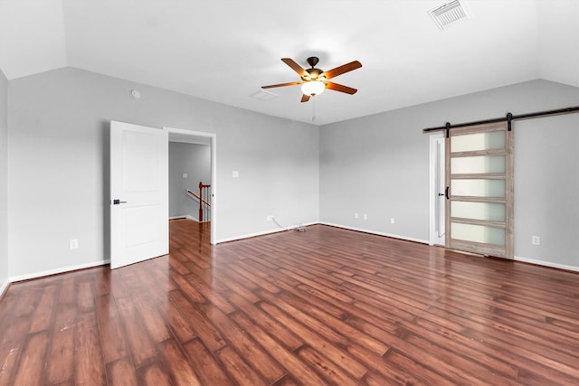 spare room featuring dark hardwood / wood-style flooring, vaulted ceiling, a barn door, and ceiling fan