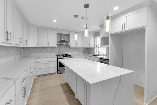 kitchen with wall chimney range hood, sink, white cabinetry, a center island, and stainless steel gas range oven