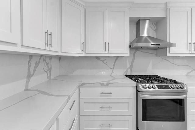 kitchen featuring light stone counters, wall chimney exhaust hood, stainless steel range with gas stovetop, and white cabinets