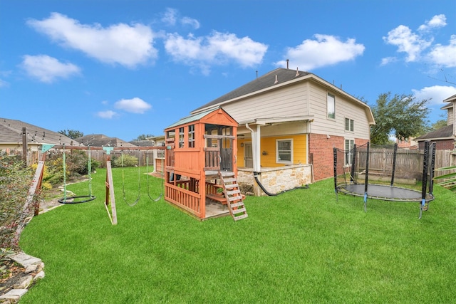 back of house featuring a trampoline, a lawn, and a playground