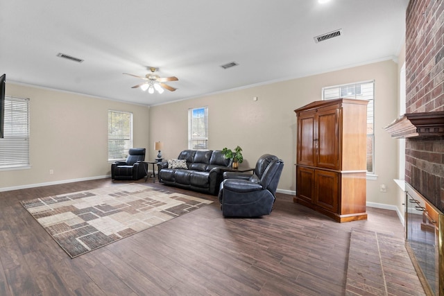 living room with a brick fireplace, crown molding, dark wood-type flooring, and ceiling fan