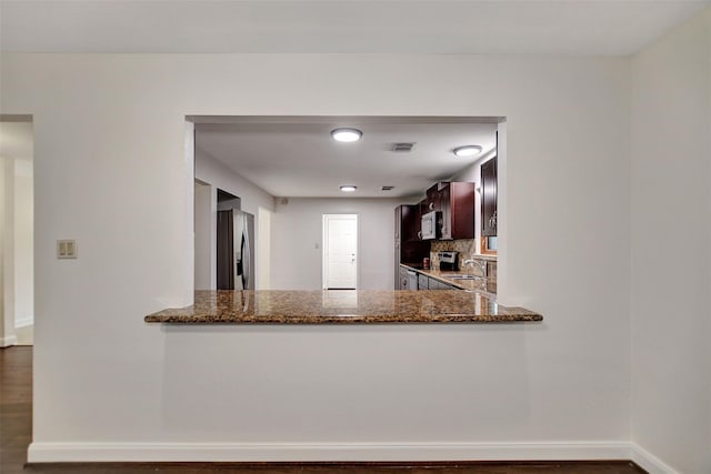 kitchen with sink, dark stone countertops, stainless steel appliances, tasteful backsplash, and kitchen peninsula