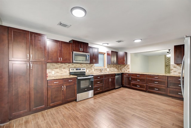 kitchen with tasteful backsplash, light stone countertops, appliances with stainless steel finishes, and light hardwood / wood-style floors