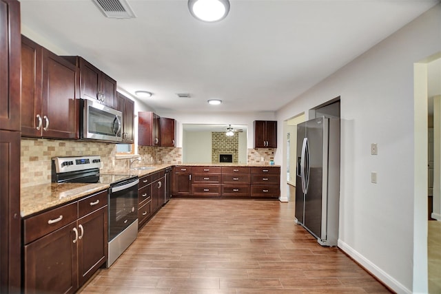 kitchen with appliances with stainless steel finishes, tasteful backsplash, sink, light hardwood / wood-style floors, and light stone countertops