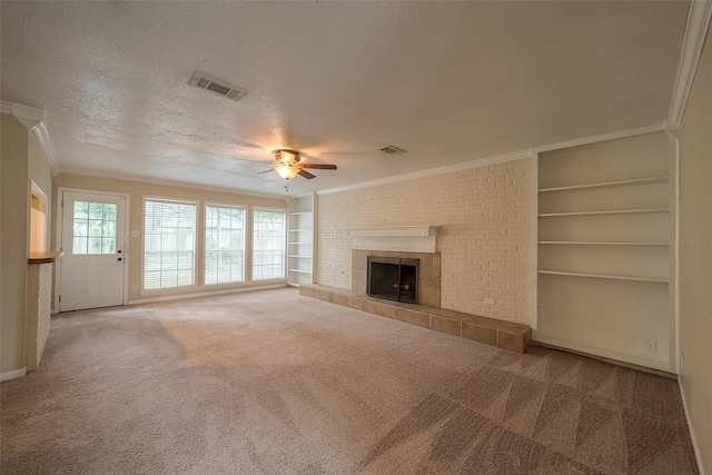 unfurnished living room featuring built in shelves, a textured ceiling, ornamental molding, carpet flooring, and a tile fireplace