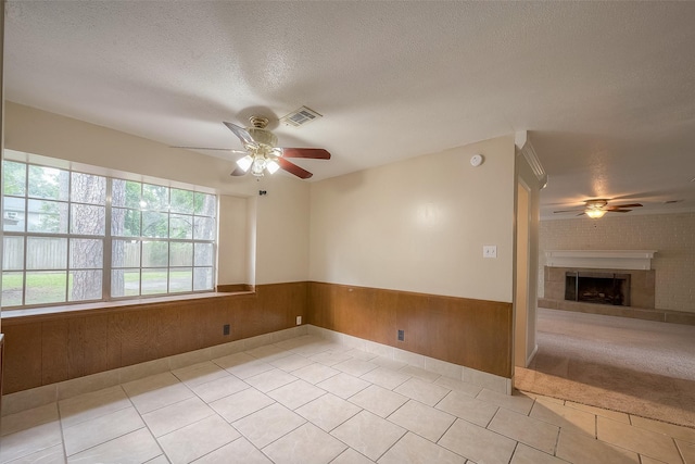 spare room featuring light tile patterned floors, a tile fireplace, ceiling fan, a textured ceiling, and wood walls