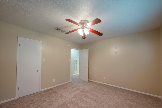 spare room with a textured ceiling, light colored carpet, and ceiling fan