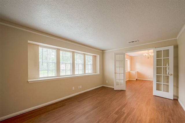 spare room featuring crown molding, wood-type flooring, a textured ceiling, french doors, and a chandelier