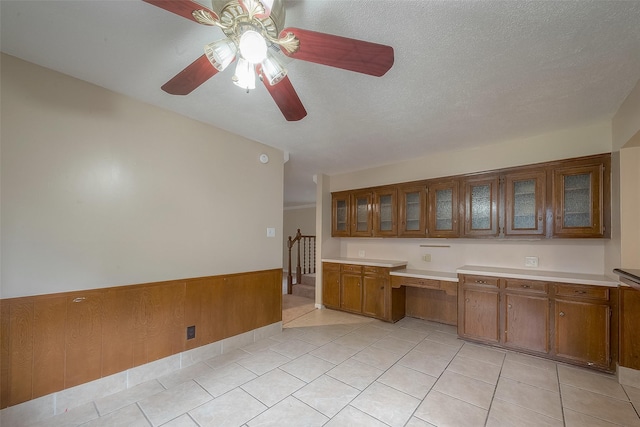 kitchen featuring light tile patterned floors, ceiling fan, built in desk, a textured ceiling, and wood walls