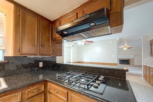 kitchen with light tile patterned flooring, exhaust hood, ceiling fan, black gas stovetop, and a textured ceiling