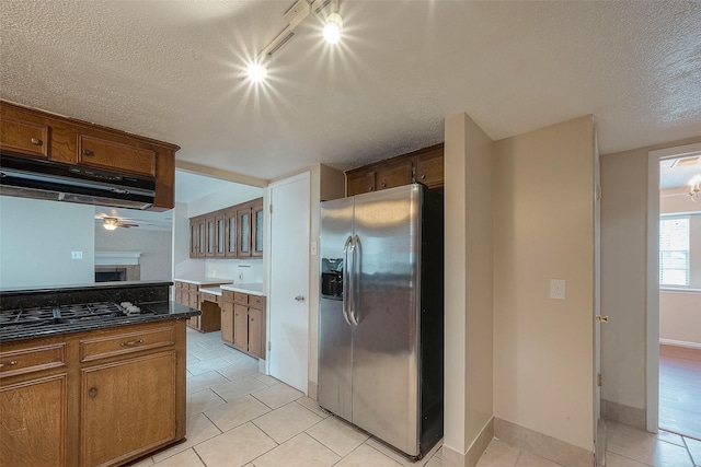 kitchen featuring dark stone countertops, stainless steel fridge, light tile patterned floors, black gas stovetop, and a textured ceiling