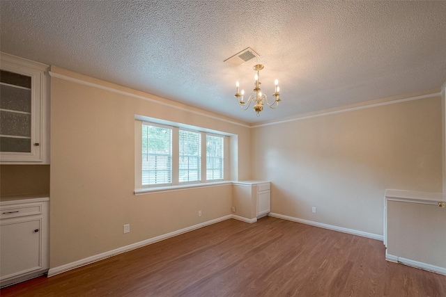 unfurnished dining area featuring an inviting chandelier, ornamental molding, a textured ceiling, and light wood-type flooring