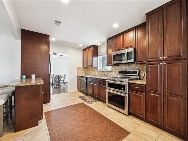 kitchen featuring light tile patterned floors, a breakfast bar area, appliances with stainless steel finishes, light stone counters, and decorative backsplash