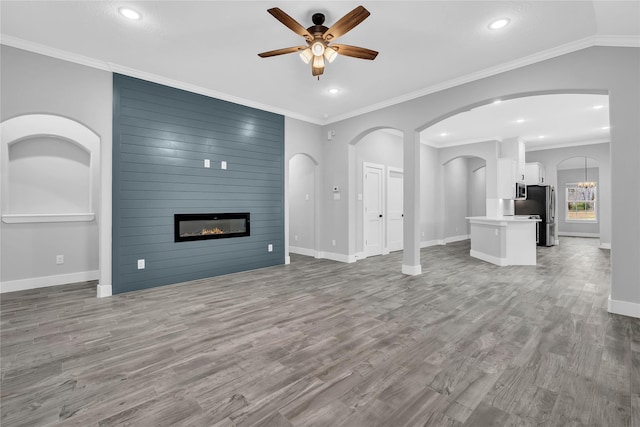 unfurnished living room with ceiling fan with notable chandelier, ornamental molding, a fireplace, and hardwood / wood-style floors