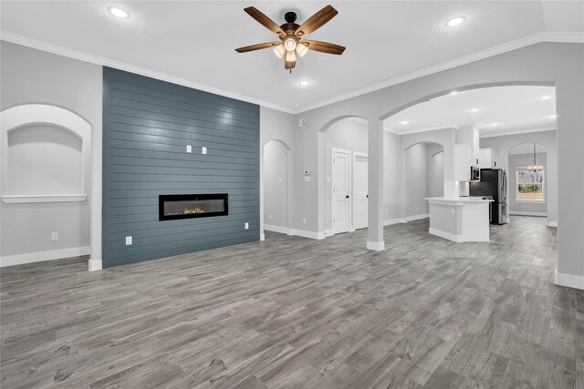 unfurnished living room with crown molding, ceiling fan with notable chandelier, wood-type flooring, and a large fireplace