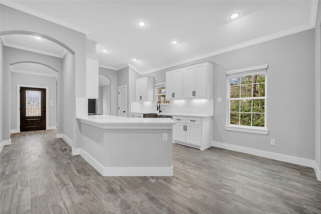 kitchen with crown molding, kitchen peninsula, light hardwood / wood-style flooring, and white cabinets