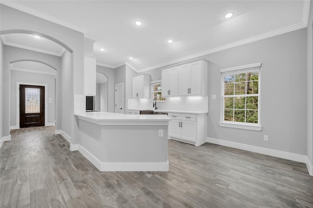 kitchen with ornamental molding, white cabinets, light wood-type flooring, and kitchen peninsula