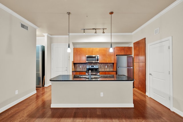 kitchen with appliances with stainless steel finishes, a kitchen island with sink, backsplash, dark hardwood / wood-style floors, and decorative light fixtures