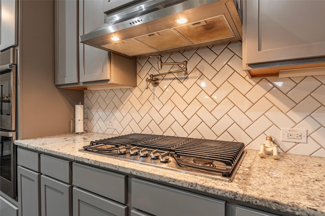 kitchen featuring extractor fan, gray cabinets, stainless steel appliances, light stone countertops, and backsplash