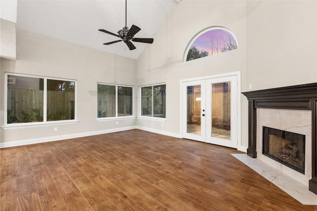 unfurnished living room with a tile fireplace, high vaulted ceiling, hardwood / wood-style flooring, ceiling fan, and french doors