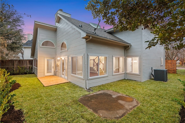 back house at dusk with a lawn and central air condition unit