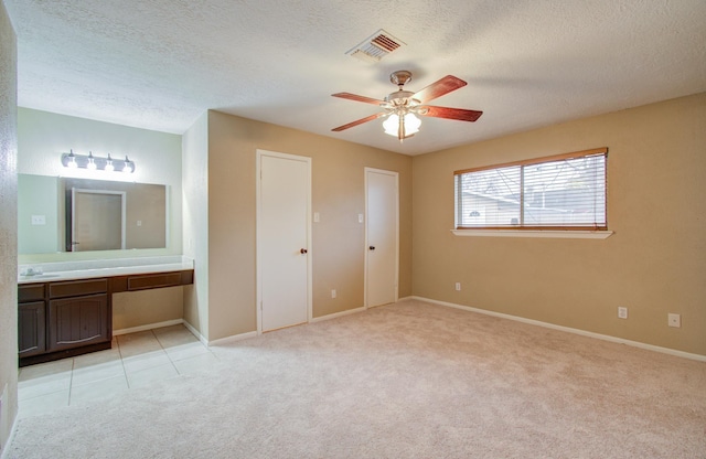 unfurnished bedroom with ensuite bathroom, sink, light colored carpet, ceiling fan, and a textured ceiling