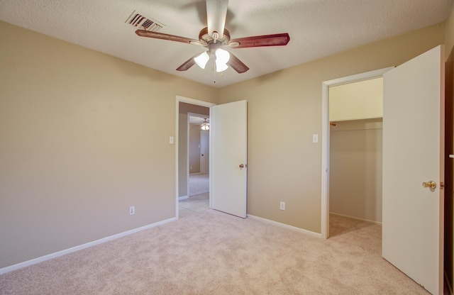 unfurnished bedroom with a spacious closet, ceiling fan, light carpet, a textured ceiling, and a closet