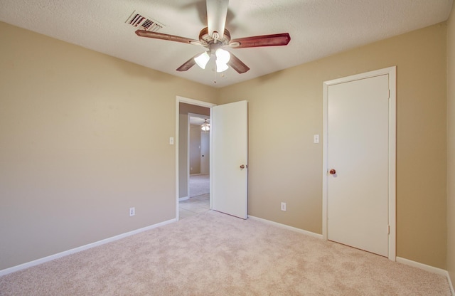 unfurnished bedroom featuring ceiling fan, light carpet, and a textured ceiling