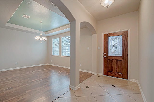 entrance foyer featuring a tray ceiling, light wood-type flooring, and a notable chandelier