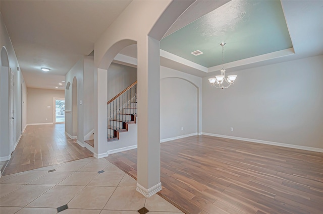 unfurnished room featuring a raised ceiling, a notable chandelier, and light wood-type flooring