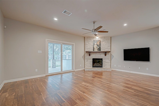 unfurnished living room featuring a stone fireplace, wood finished floors, visible vents, baseboards, and a ceiling fan