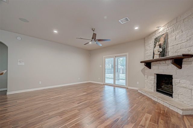 unfurnished living room featuring hardwood / wood-style floors, a stone fireplace, and ceiling fan