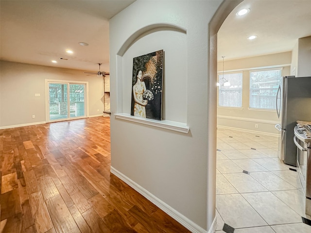 hallway featuring arched walkways, recessed lighting, light wood-type flooring, and baseboards