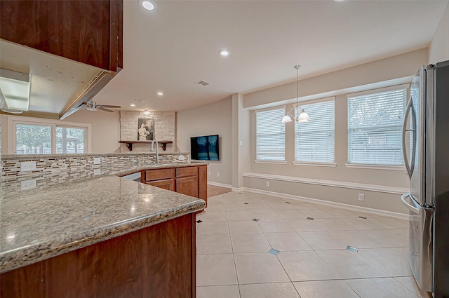 kitchen with stainless steel refrigerator, sink, decorative backsplash, hanging light fixtures, and light stone counters